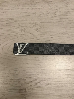 Rutigt svart bälte med material av läder  - Snyggt bälte med klassiskt rutigt mönster i svart och grått samt ett stilrent -spänne i silver. Bältet har en insida i ljust brunt skinn och är 110 cm långt. Perfekt accessoar för att lyfta din outfit.