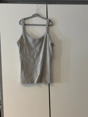 Grått ribbat linne - Säljer ett enkelt och stilrent grått linne med breda axelband och rundad halsringning. Linnet är ribbstickat och har en kroppsnära passform, perfekt att matcha med jeans eller kjol.