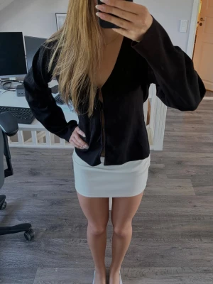 Svart v-ringad topp - Svart blus med v-ringning och knappar framtill. Långärmad modell i mjukt tyg som ger en clean och modern look. Perfekt att styla med kjol eller jeans för en trendig vibe.