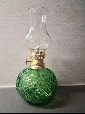 Grön oljelampa i glas - Säljer en vintage oljelampa med rund, mönstrad grön glaskropp och klassisk mässingsfärgad brännare. Lampan har en genomskinlig glaskupa med elegant form. Perfekt som dekoration eller mysbelysning i hemmet. 20 cm hög