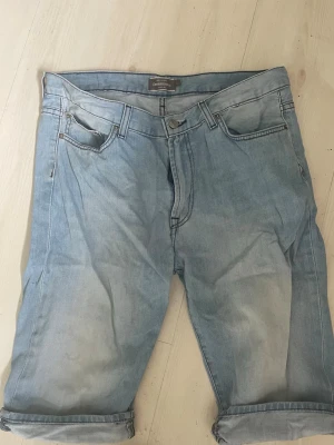 Dressman Ljusblå jeansshorts med uppvik - Säljer ett par Dressman  ljusblå jeansshorts med klassisk femficksdesign och uppvikta benslut. Shortsen har normal passform och stängs med knapp och dragkedja. Perfekta för varma dagar och enkla att matcha med olika stilar.
