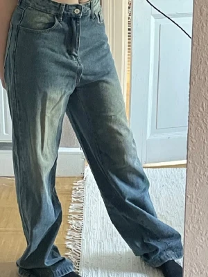 Baggy jeans med tryck bak - Säljer ett par blå baggy jeans med coolt gult tryck på bakfickorna och över rumpan. Jeansen har hög midja, raka ben. Materialet är denim och passformen är avslappnad och loose fit. Perfekta för en streetwear-look.