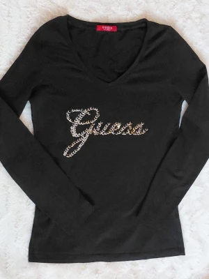 Y2K Guess paljettopp - Snygg svart långärmad topp från Guess med v-ringning och paljetter som bildar loggan på bröstet. Snygg passform och i gott skick, hittar inga defekter. Hör av dig vid frågor❤️