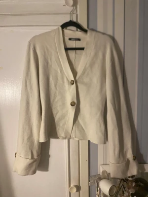 Beige kofta/kavajliknande topp – Gina Tricot (S) - Superfin beige topp från Gina Tricot i storlek S. Feminint snitt med lätt markerad midja och dekorativa knappar framtill. Perfekt blandning mellan kofta och lättare kavaj 🤍 • V-ringning • Två knappar framtill • Långa ärmar med fina uppvik och knappdetalj • Mjuk och skön kvalitet • Smickrande passform Passar perfekt till jeans, kostymbyxor eller kjol – både till vardag och mer uppklätt. Väldigt fin neutral färg som matchar allt ✨ Säljes då den inte används. Kan visa bild på🤍