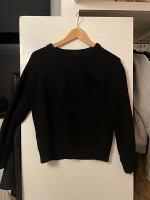 Svart stickad tröja från Vila - En enkel och stilren svart stickad tröja från Vila. Tröjan har rund halsringning, långa ärmar och ribbade muddar vid hals, ärmslut och nederkant. Perfekt basplagg till garderoben och lätt att matcha med olika outfits. Liten M . Finns päls på den 