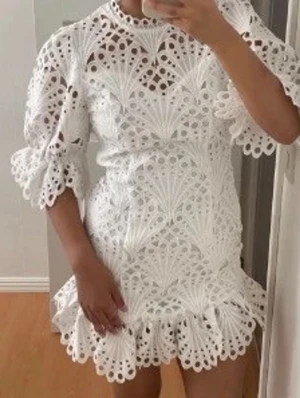 Vit spetsklänning med volang - Superfin vit kortklänning i spets med puffiga trekvartsärmar och volangkant nedtill. Klänningen har ett detaljerat broderat mönster och rund halsringning. Perfekt till student eller sommarens fester.
