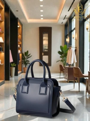 Mörkblå handväska från Estuti Bags - Snygg mörkblå handväska i slät konstläder med stilren boxig form. Väskan har två korta handtag och en avtagbar axelrem med guldfärgade detaljer. Perfekt för dig som gillar en klassisk och modern look.