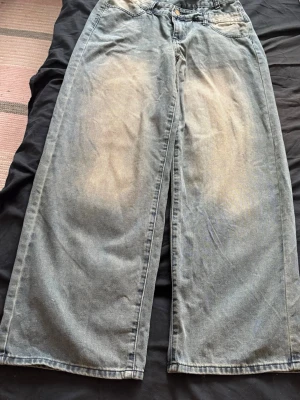 Blåa wide leg jeans med slitningar - Säljer ett par blåa wide leg jeans med ljusa slitningar framtill och baktill. Jeansen har hög midja, klassisk femficksmodell och raka, extra vida ben. Perfekta för en avslappnad och trendig look.