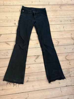 Svarta bootcut jeans med rå kant - Säljer ett par svarta bootcut jeans med rå, fransig kant nedtill. Jag har sprättat ner dem i benen, ordinarie storlek är 30 men nu är de ca 2 cm längre. Jeansen har klassisk femficksmodell och normal midja. Materialet är stretchigt denim som sitter snyggt och bekvämt. Perfekta för dig som gillar en avslappnad men trendig look.