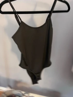 Svart body med smala axelband - Snygg svart body med justerbara smala axelband och enkel, stilren design. Materialet är troligtvis syntetiskt och känns mjukt och stretchigt. Klassisk passform med rundad halsringning och hög benskärning.