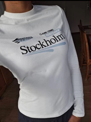 Vit långärmad topp Stockholm-print - Vit långärmad topp med trycket 'Stockholm' och grafiska detaljer i svart och ljusblått framtill. Aldrig använd. 