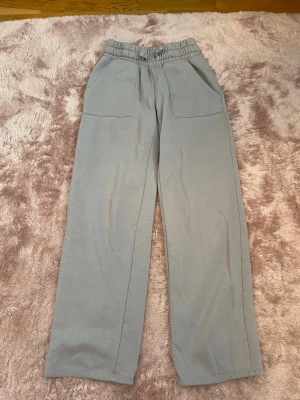 Grå mjukisbyxor från 157 - Säljer ett par grå mjukisbyxor från 157 med bred resår i midjan och två stora fickor framtill. Byxorna har raka ben och är gjorda i mjukt, bekvämt material som passar perfekt för chill dagar. Enkel och stilren design som är lätt att matcha. XS 