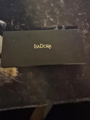 Isadora ögonskuggspalett med 32 färger - Snygg ögonskuggspalett från Isadora med 32 olika färger, inklusive blå, grön, rosa, brun, beige och guldtoner. Paletten har en rektangulär svart förpackning och inkluderar en dubbeländad borste. Perfekt för att skapa kreativa och färgstarka ögonlooks.