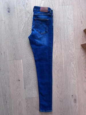 Blå skinny jeans från Samsøe Samsøe - Snygga blå skinny jeans från Samsøe Samsøe med klassisk femficksdesign och läderpatch bak i midjan. Jeansen har en smal passform och är gjorda i mjukt denimtyg med lite stretch för extra komfort. Modell Alice jeans. Stl W27 L32.