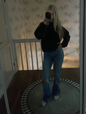 Blå bootcut jeans med hål på knät - Säljer ett par blå bootcut jeans med slitning och hål på ena knät. Jeansen har klassisk femficksdesign och är i ett mjukt denimtyg. Perfekta för en avslappnad och trendig look.