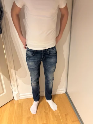 Dondup George skinny fit  - Säljer ett par Dondup George blåa jeans med snygga slitningar och tvättade detaljer. Jeansen har klassisk femficksmodell, låg midja och knappgylf. Perfekta för en avslappnad och trendig look. Materialet är denim i bomull.