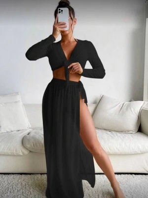 Svart strandset med lång kjol & topp - Snyggt svart strandset med lång kjol med hög slits och matchande långärmad knyt-topp. Setet har en trendig och luftig design, perfekt att bära över baddräkt eller bikini. Materialet är lätt, vilket ger en bekväm känsla.