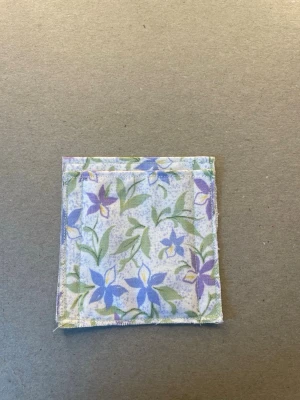 Blommigt tygfodral med uggleberlock - Säljer ett liten plånbok av tygfodral i vitt med lila och gröna blommor. På ena hörnet sitter en liten silverfärgad uggleberlock som detalj. Perfekt för småsaker eller som accessoar i väskan. Säljs med eller utan detalj. 8,5 cm hög, bredd  8,1 cm. Sytt in så perfekt storlek för kort. Handgjord