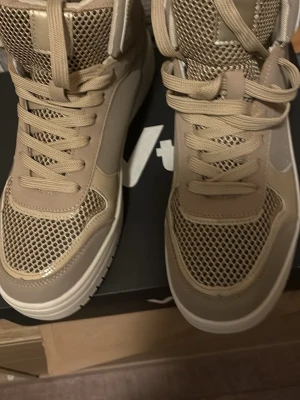 Beige mesh high-top sneakers - Snygga high-top sneakers i beige med meshdetaljer och matchande snörning. Skorna har en chunky sula och cool design som sticker ut. Perfekta för dig som vill ha en modern och sportig look. Materialmix av mesh och syntet för extra komfort.