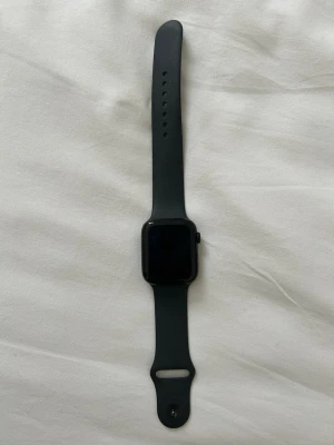 Svart Apple Watch med silikonarmband - Snygg svart Apple Watch med rektangulär skärm och matchande svart silikonarmband. Klockan har en modern och stilren design med digital krona på sidan. Perfekt för dig som vill ha koll på notiser, träning och hälsa direkt på handleden. 44 mm Appel Watch se gen 2 (gps + cellular) igen tecken på användning haft den cirka en månad men aldrig användt den cirka 4500 i nypris 
