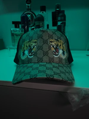 Tiger keps  - Säljer en snygg keps med klassiskt GG-mönster och två stora tigerhuvuden framtill. Kepsen har beige och bruna toner, svart mesh på sidorna och justerbar baksida. Perfekt för dig som vill sticka ut med en lyxig och trendig accessoar