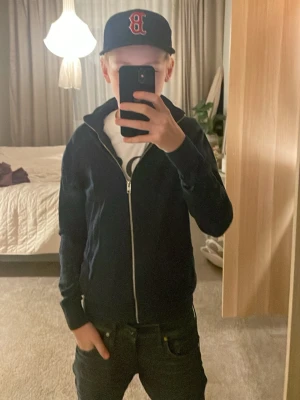 Mörkblå ziptröja från J.Lindeberg - Snygg mörkblå ziptröja från J.Lindeberg med hel dragkedja framtill och hög krage. Tröjan har en stilren design och är tillverkad i ett mjukt material som passar perfekt till vardags. Långa ärmar och ribbade muddar ger en clean look.