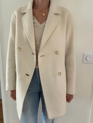 Offwhite ullkappa Uniqlo stl XS - Offwhite/cremevit dubbelknäppt  kort kappa med krage och två fickor framtill. Kappan har en rak passform och knäpps med två knappar framtill. Ullmix. Stl XS. Rak lite oversize modell. Använd några gånger, inga defekter men är lätt smutsig på några ställen men inget jag tycker behöver tvättas ännu.  Nypris: 1499kr