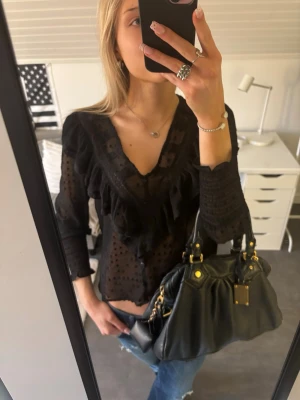 Svart blus med volanger - Trendig svart blus i transparent mesh med prickigt mönster och volangdetaljer längs ringningen.  Perfekt att styla med jeans eller kjol för en cool outfit.