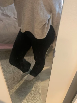 Svarta jeans med speciella fickor - Säljer ett par svarta jeans med utsvängda ben och snygga broderade detaljer på bakfickorna. Jeansen har ficklock med knappstängning och är tillverkade i ett mjukt, bekvämt material. Perfekta för dig som vill ha en unik touch på din outfit.