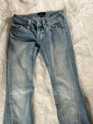 True religion  - Säljer ett par ljusblå bootcut jeans från true religion med klassisk femficksdesign och snygga slitningar. Jeansen har låg midja, och är i perfekt skick! Jeansen har förrut sytts kortare, men det är inget som märks eller syns, dessa är i storek w23.