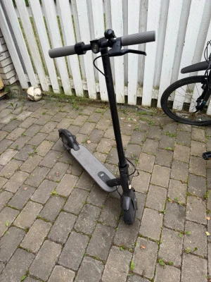 Xiaomi Elscooter 1S - Säljer en svart elsparkcykel med grått deck och handtag. Stilren design med bred fotplatta och framlykta. Perfekt för att ta sig runt i stan eller till skolan. Laddningsuttag finns på sidan av decket och styret har en enkel display.