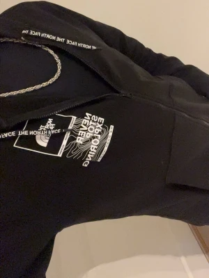 Svart hoodie från The North Face M - Säljer en svart hoodie från The North Face med vit logga och tryck på bröstet. Hoodien har dragkedja, huva med snörning och en klassisk streetwear-look. Perfekt för dig som gillar stilrena och bekväma plagg.
