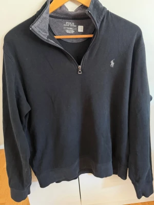 Svart halvzip från Polo Ralph Lauren - Klassisk svart långärmad tröja från Polo Ralph Lauren med halv dragkedja och broderad logga på bröstet. Tröjan har ribbade muddar och är tillverkad i mjuk bomullsblandning. Säljer den då den är för kort för mig, den är köpt för 2295kr på zalando o använd max 5 gånger så den är i väldigt bra skick, pris ej hugget i sten!🪨 