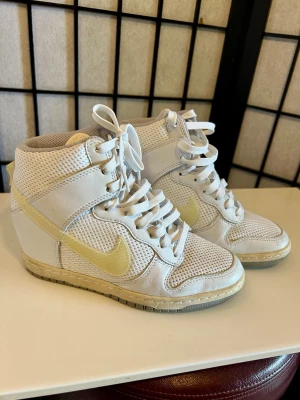 Nike Dunk Sky Hi Wedge 🤍✨ - Nike Dunk Sky Hi med dold kilklack – en riktig Y2K-klassiker 🤍✨  Vit mesh och läder med creamfärgade detaljer. Perfekta till baggy jeans, kjol eller cargos. Ovanligare modell som blivit populär igen tack vare Y2K- och 2010-talstrenden.  • Storlek 35.5 • Dold kilklack • Y2K / Tumblr / Indie Sleaze • Fint använt skick  📦 Skickas snabbt 💬 Bud & bundle välkomnas
