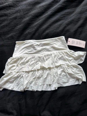 Vit volangkjol från Nelly - Supersöt vit kortkjol från Nelly med dubbla volanglager som ger en flowy och lekfull look. Kjolen är gjord i mjukt material och har en bred midjeresår för skön passform. Perfekt att styla med en crop top eller oversized hoodie. Den är i nyskick och aldrig använd!💕