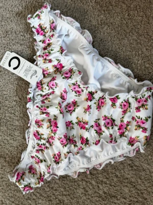 Vit blommig bikiniunderdel C SWIM - Superfin bikiniunderdel från C SWIM i vitt med rosa blommigt mönster och volangdetaljer längs kanterna. Materialet är stretchigt och bekvämt, perfekt för strand och pool under sommaren. Aldrig använd med prislapp kvar. 💕