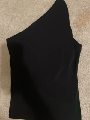 Svart oneshoulder topp - Snygg svart topp med oneshoulder-design. Enkel och stilren modell som passar perfekt till jeans eller kjol. Helt oanvänd perfekt till fest eller en vanlig dag! 