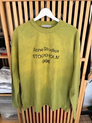 Grön långärmad topp Acne Studios - Cool långärmad topp från Acne Studios i en unik grön nyans med trycket 'Acne Studios STOCKHOLM 1996' på bröstet. Rund halsringning och avslappnad passform. Perfekt för dig som gillar streetwear och skandinavisk design. Storlek M och i oanvänt skick.