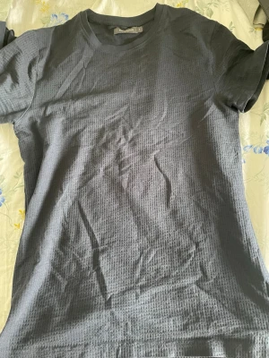 Mörkblå ribbad t-shirt Dressmann - Snygg mörkblå t-shirt från Dressmann med ribbad struktur. Klassisk rund halsringning och korta ärmar. Perfekt basplagg som funkar till allt och är riktigt skön tack vare sitt mjuka bomullsmaterial.