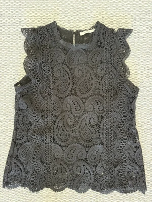 Svart spetsblus  - Säljer en svart ärmlös spetsblus. Blusen har rund halsringning och knäppning bak. Perfekt för dig som gillar unika och snygga toppar med mycket detaljer🖤🐈‍⬛Storlek M men skulle säga att den är mindre i storlek pch sitter mera som en S.