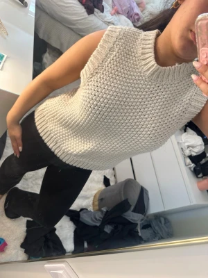 Beige stickad ärmlös topp - Säljer en beige stickad topp med grov struktur och hög hals. Toppen är ärmlös och har en avslappnad passform som är perfekt för lager på lager. Enkel och stilren design som passar till det mesta.
