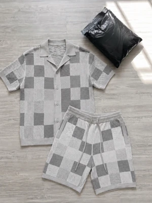Gråvit rutig kortärmad topp - Snygg kortärmad topp i grått och vitt med rutigt mönster och knappar framtill. Skön krage och avslappnad passform, perfekt till sommaren. Materialet känns mjukt och andas bra, troligen bomull eller polyester.
