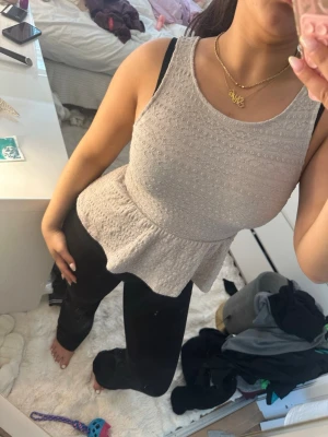 Beige ärmlös peplumtopp - Snygg beige ärmlös peplumtopp med rund halsringning och diskret strukturmönster. Toppen har en markerad midja och volang nedtill som ger en feminin siluett. Perfekt att styla med både jeans och kjol.