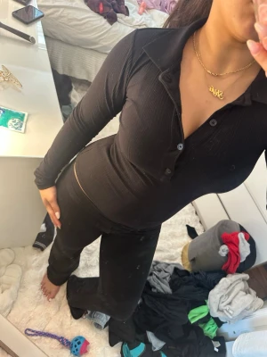 Svart ribbad tröja - Mysigt svart loungewear-set med långärmad ribbad topp . Toppen har knappar framtill och en djup v-ringning. Perfekt för chill dagar hemma eller när du vill vara bekväm men ändå se snygg ut.