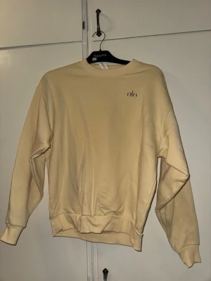 Beige sweatshirt från Alo - Snygg beige sweatshirt från Alo med rund halsringning och diskret logga på bröstet. Tröjan har en loose passform och ribbade muddar vid ärmslut och nederkant. Perfekt för en avslappnad och trendig look.