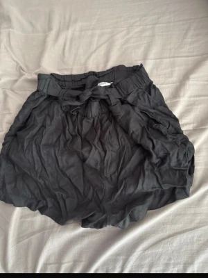 Svarta loose shorts med knyt - Säljer ett par svarta shorts från Kappahl  med loose passform och hög midja. De har ett snyggt knytband i midjan och är tillverkade i mjuk bomull, perfekt för varma dagar. Stilen är enkel och avslappnad, med bred resår upptill för extra komfort. Storlek 164 men funkar för större