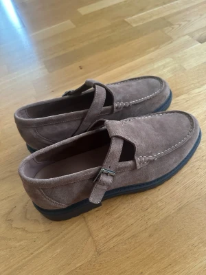 Zara  nytt Bruna mocka seglarskor med spänne  - Säljer ett par stilrena seglarskor i brun mocka med coolt spänne på sidan. Skorna har en klassisk loafer-form med kontrastsömmar och svart sula. Perfekta för dig som gillar en avslappnad men ändå snygg look.