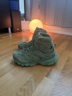 Balenciaga Track Highs i olivgrönt - Säljer ett par Balenciaga Track sneakers i olivgrönt. Skorna har en chunky sula, högt skaft och detaljerad paneldesign i mesh och syntetmaterial. Balenciaga-logga på sidan och 'track' på hälen. Perfekta för dig som gillar statement sneakers.