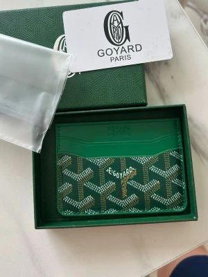 Goyaard Plånbok - Grön - Snyggt och exklusivt kortfodral från Goyard i grön färg med klassiskt mönster och logotyp. Tillverkad i läder och har flera fack för kort. Perfekt för dig som vill ha något stilrent och lyxigt att bära med dig. Box och kort medföljer.