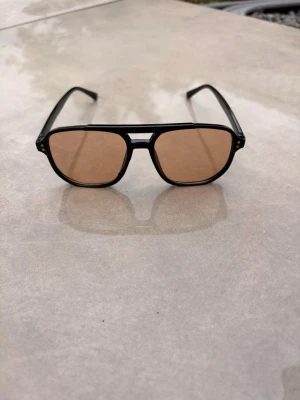 Svarta pilotbågar solglasögon - Snygga solglasögon med svarta pilotbågar och bruna tonade glas. Klassisk aviator-form som ger en cool vibe och passar till de flesta outfits. Ramen är i plast och glasen har en lätt brun ton som skyddar mot solen.🕶️☀️⛱️